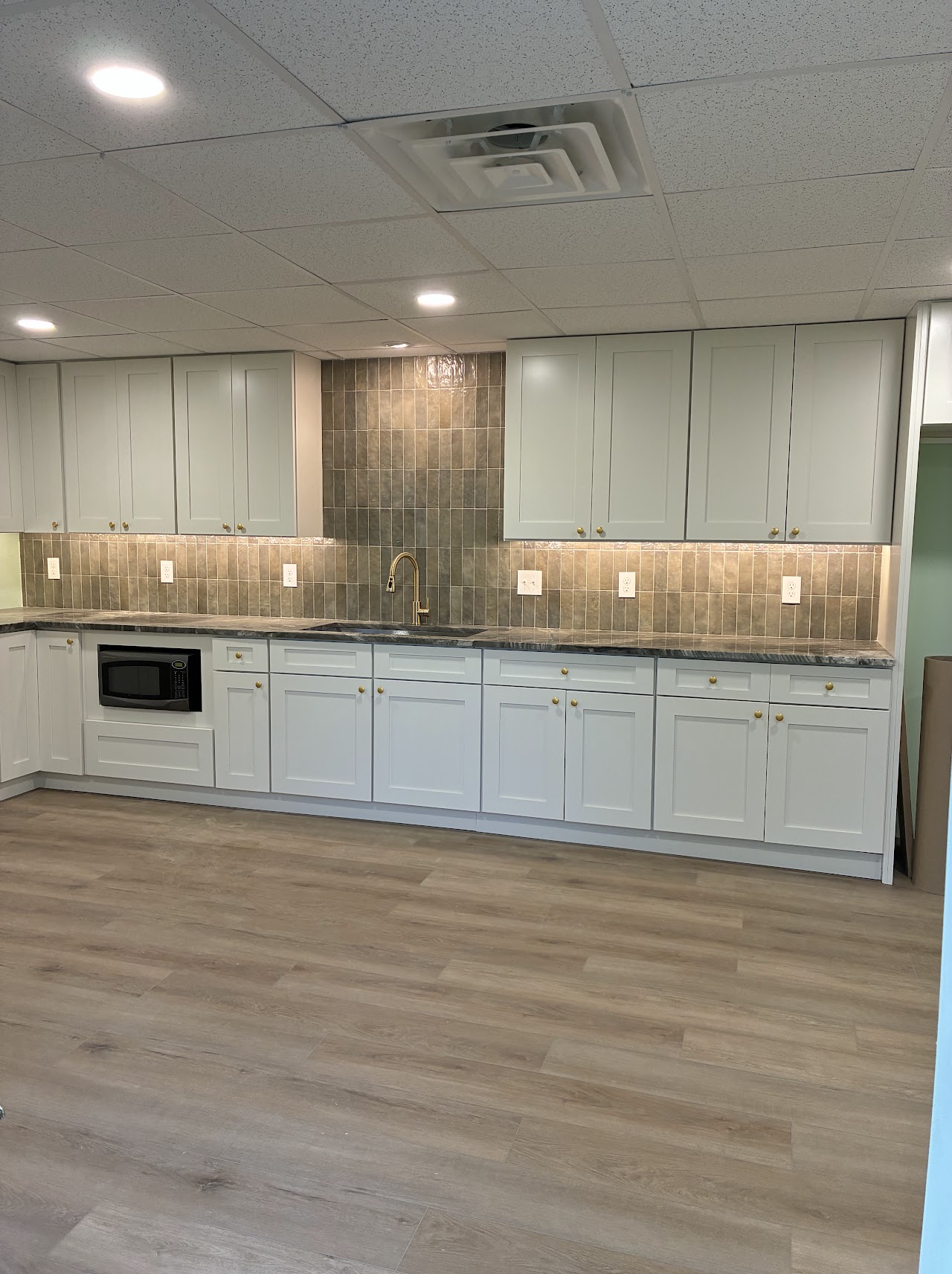 A long run of white kitchen cabinets under a tiled backsplash, new plank floor in front
