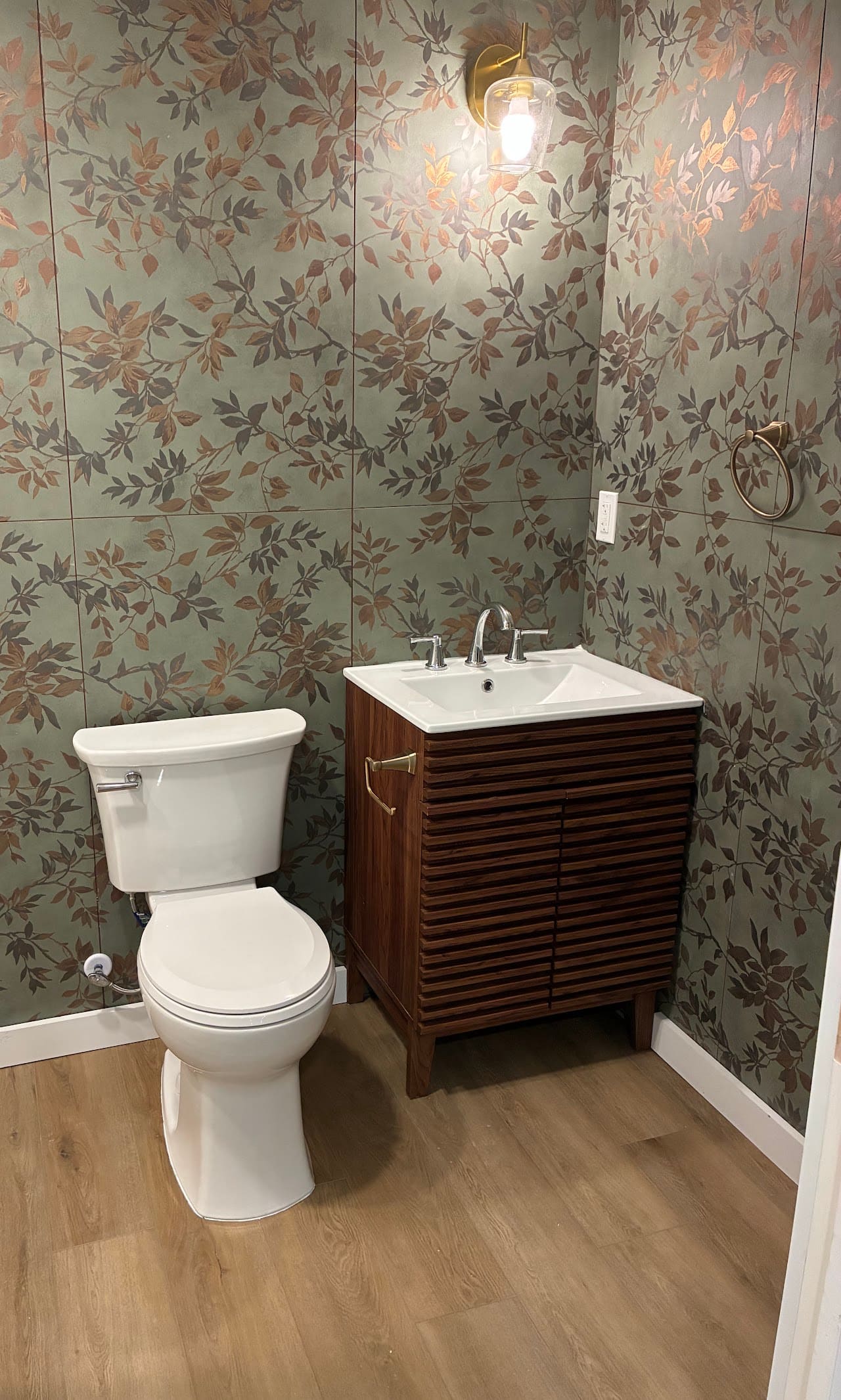 A powder room finished in patterned floral wallpaper with a walnut vanity