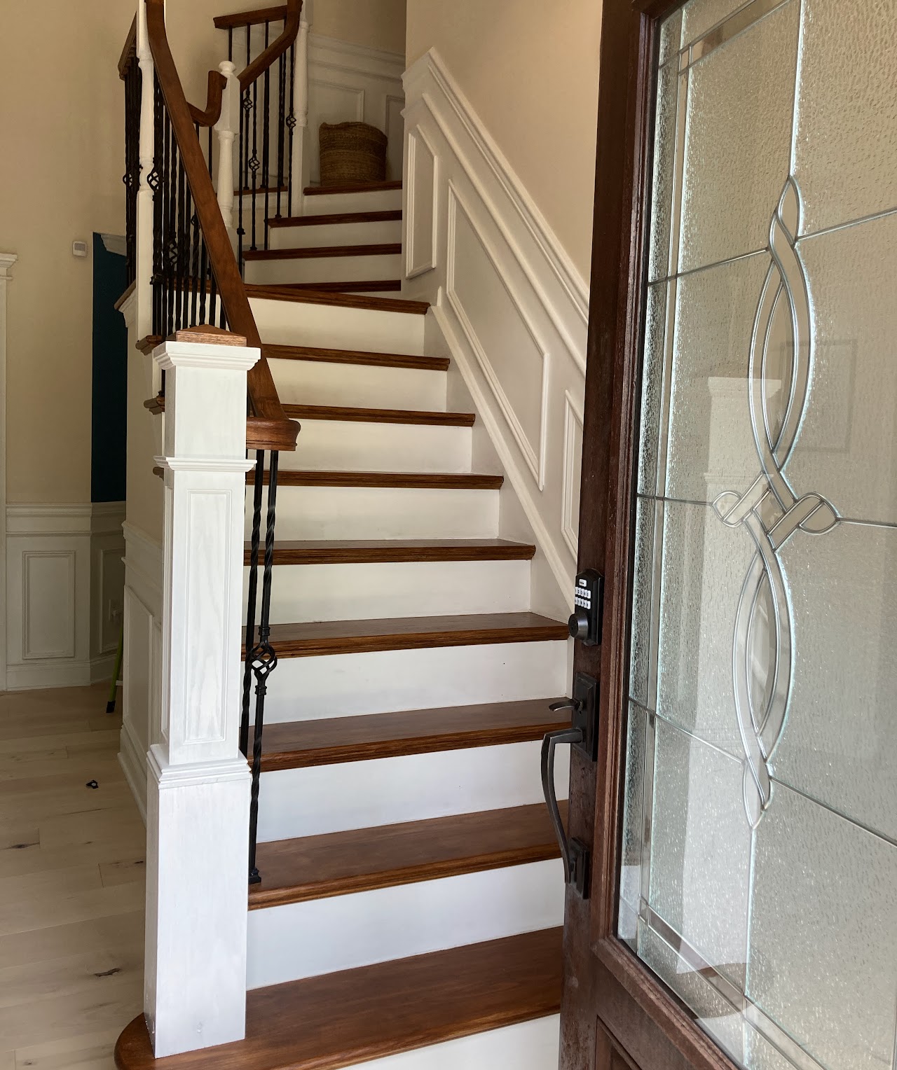A wood-tread stair with white panelling beside a leaded glass front door